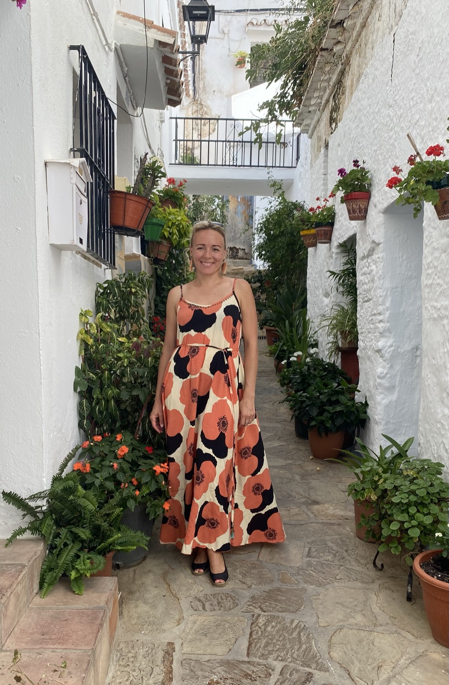 The author standing in a narrow whitewashed street lined with potted plants